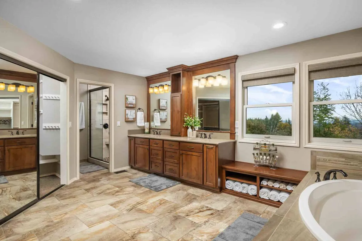 A spacious, modern bathroom featuring a double sink vanity, large mirror, bathtub, shower area, and windows that offer lovely views. The design is serene and rejuvenating, with a spa-like ambiance ideal for unwinding after a day of adventure.