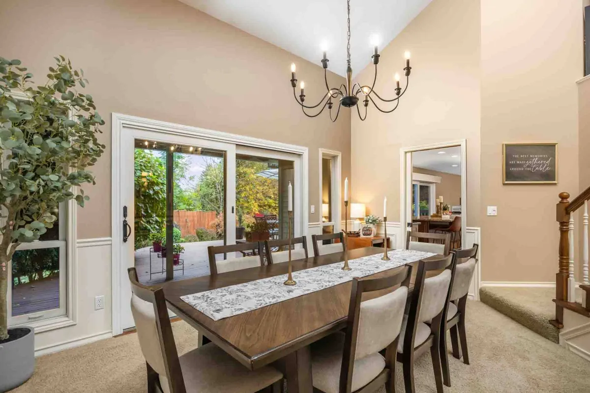 A view of the spacious dining area with a large table, elegant chandelier, decorative plant, and expansive windows that bathe the space in natural light and offer views of the private, verdant grounds.