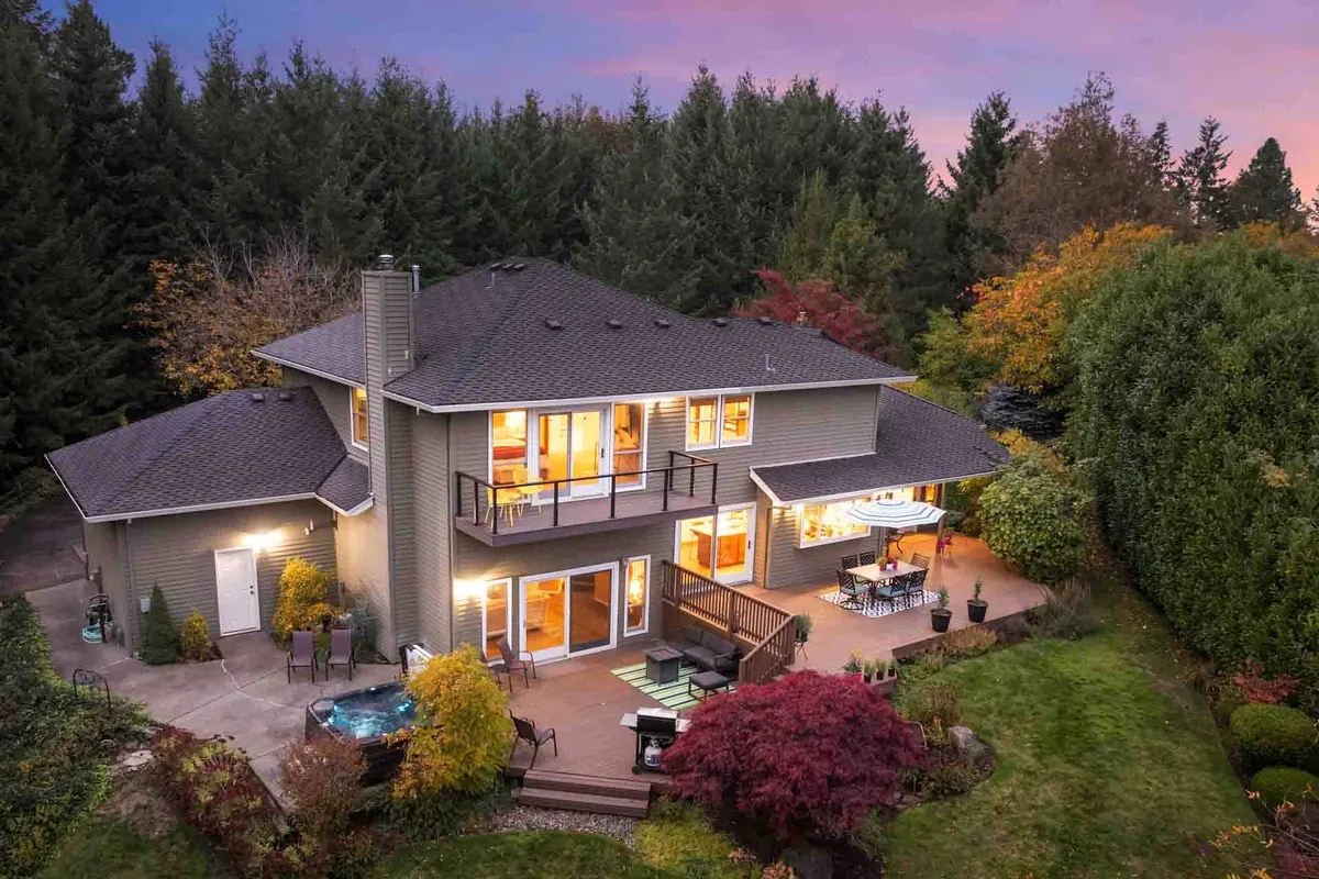 The image showcases a beautiful single-family house set on five sprawling acres, with a spacious deck overlooking lush gardens and a relaxing hot tub inviting guests to unwind. The tranquil setting is perfect for enjoying sunsets, entertaining outdoors, or stargazing in the evening—all framed by the serene Oregon landscape.