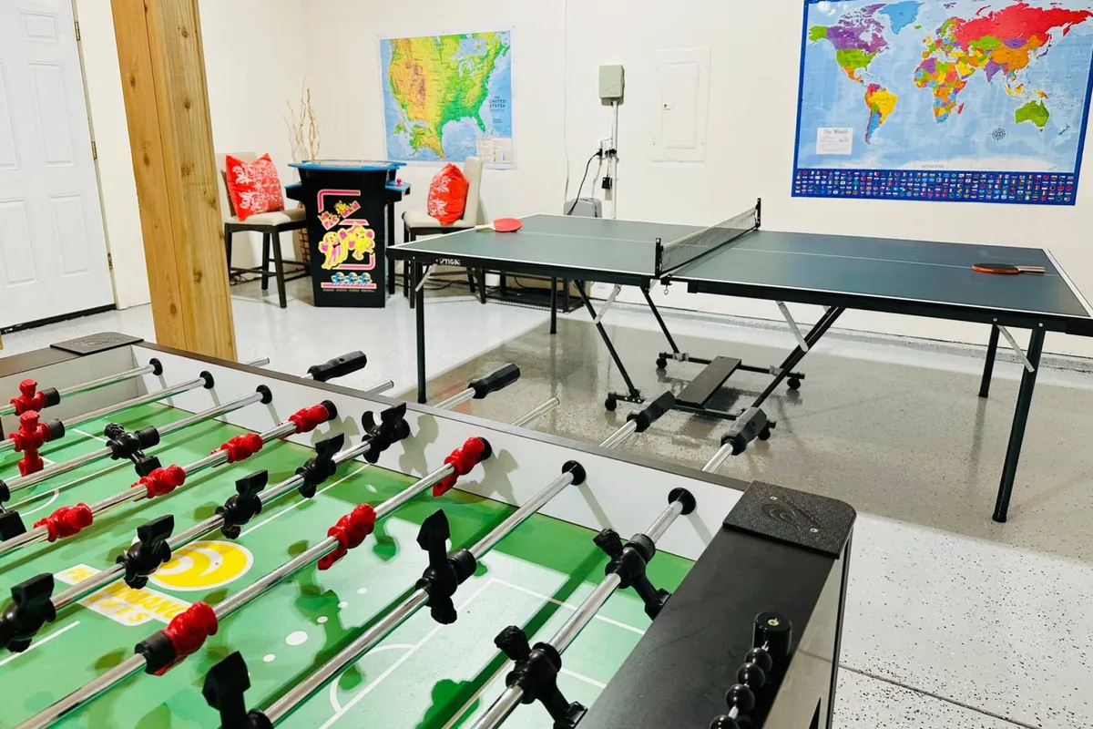 A vibrant game room with a foosball table, ping pong table, a colorful world map on the wall, cheerful chairs, and an arcade machine in view. The layout is open and inviting, encouraging multiple activities at once, with space for movement and socializing.