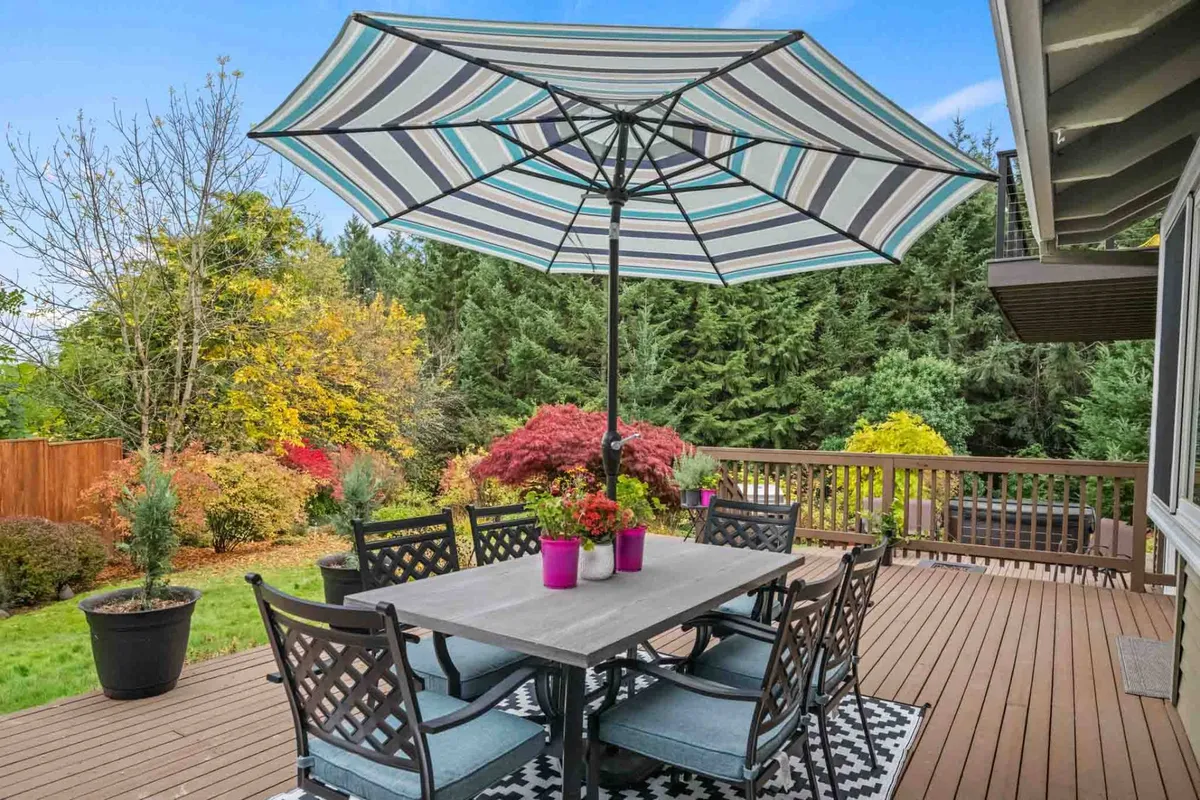 A vibrant outdoor dining area featuring a large striped umbrella, a spacious table with chairs, and an abundance of colorful potted plants. This cheerful setting is ideal for group meals or celebrations, perfectly matching the section's mention of family meals and relaxed gatherings outdoors.