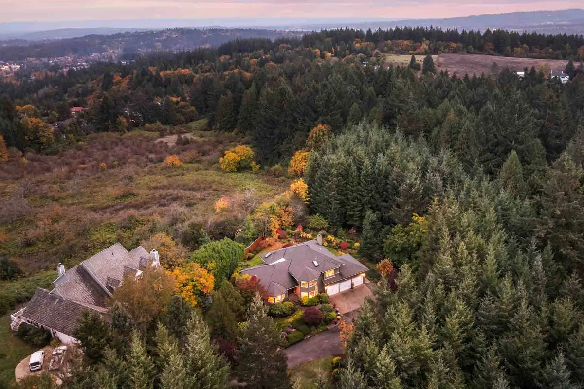 This exterior image showcases the main house surrounded by mature trees and vibrant, colorful foliage. The expansive lawn and natural landscape evoke the feeling of being immersed in nature, perfect for families seeking open spaces to play, explore, and unwind. The tranquil setting hints at the sprawling five-acre property mentioned in the section, inviting both adventure and relaxation.