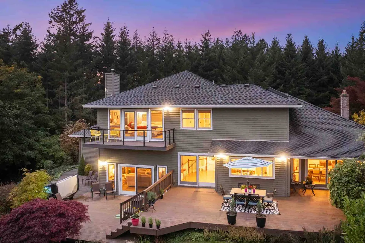 This image features a spacious deck area with comfortable outdoor seating, a patio table, and a landscaped garden. Large windows connect the indoor and outdoor spaces, creating a seamless transition for relaxation and gatherings. The deck is set up to enjoy scenic views and sunsets, evoking a sense of romance and leisure.