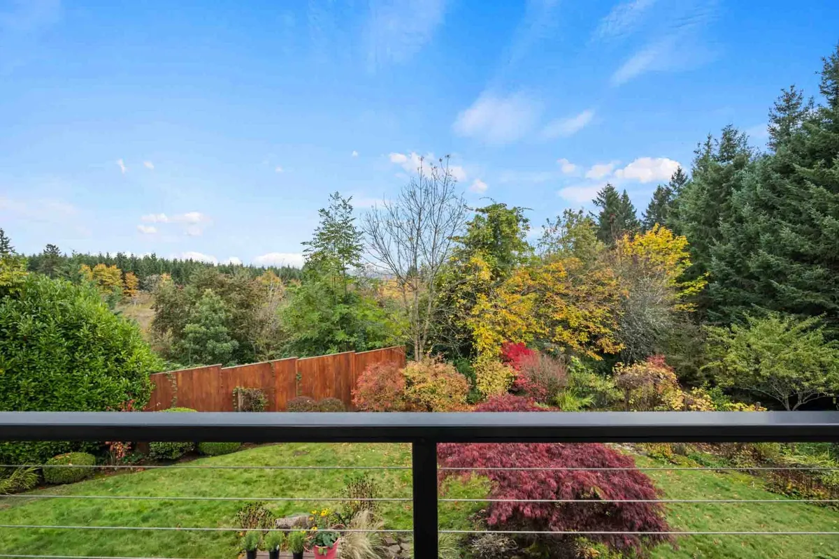 A panoramic view of a lush green lawn bordered by vibrant autumn trees and a wooden fence. The scene is open and calm, capturing the essence of seasonal changes and the peacefulness of the surrounding landscape.