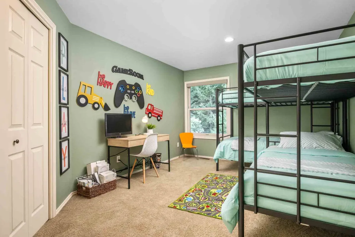 A playful and functional bunk room setup with bunk beds, gaming console-themed wall art, and a desk with computer, creating an ideal space for children to sleep, play, and study. The color scheme and decor are energetic and fun, appealing to families and young guests.