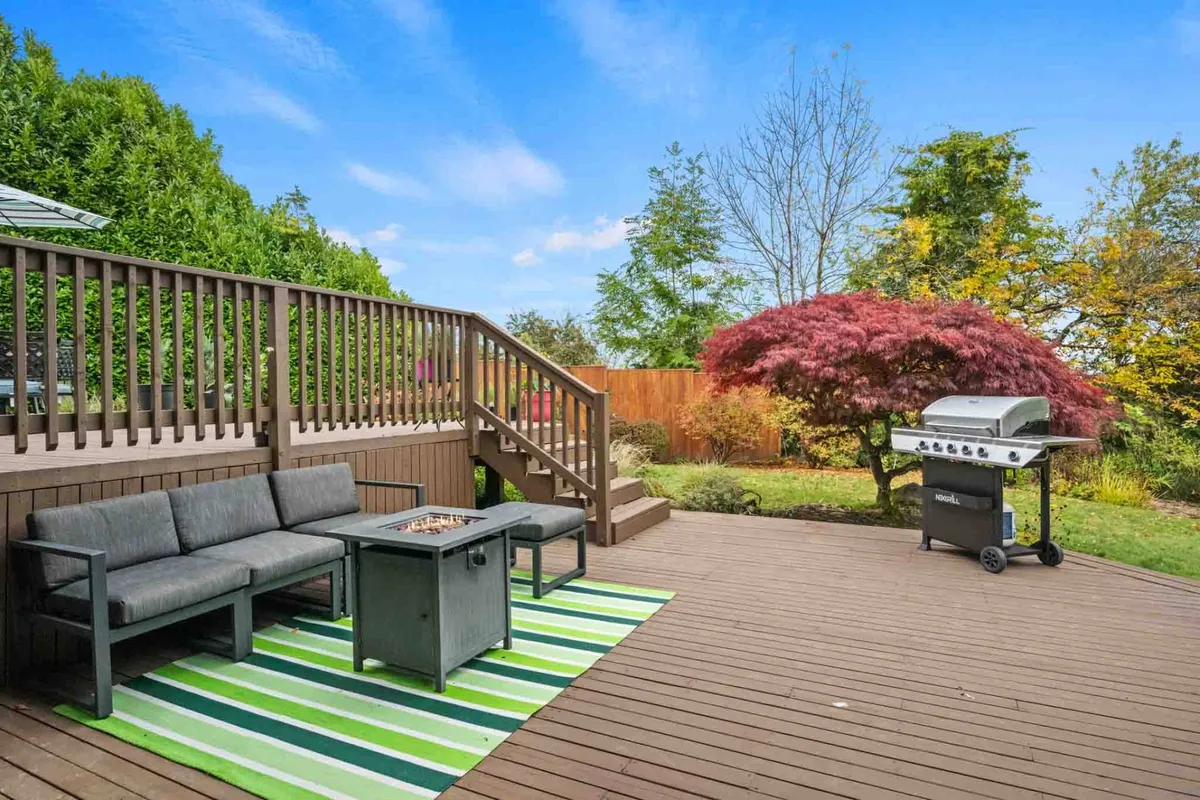 The image shows an inviting outdoor seating area with comfortable chairs, a grill, and a decorative tree. It evokes a casual, social mood ideal for gatherings, morning coffee, or sunset barbecues on the deck.