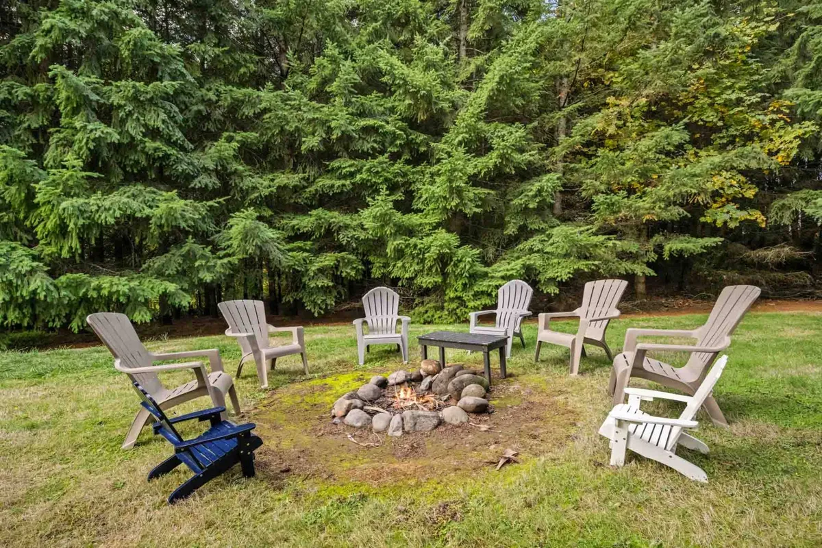 A cozy fire pit area, complete with wooden chairs and nestled among tall trees, creates an inviting spot for families to gather in the evenings. The communal setup is perfect for storytelling, marshmallow roasting, or simply enjoying the calm of the outdoors after a day of adventure at the park.